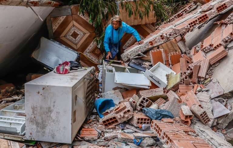 Uma pessoa está no meio de escombros de uma casa destruída pelas chuvas